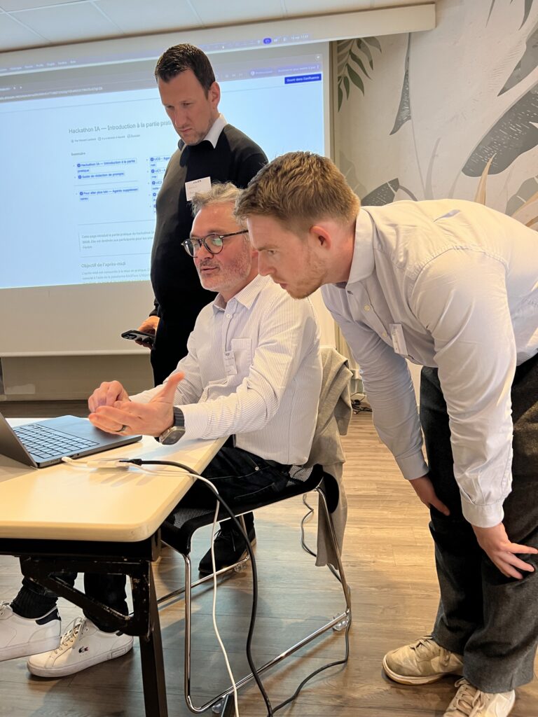 Deux participants penchés sur un poste de travail, l’écran de consignes du hackathon en arrière-plan.